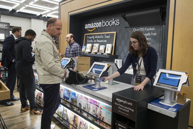 In this Thursday, May 25, 2017, photo, a salesperson helps a customer use his smartphone to make a payment at the Amazon Books store in the Time Warner Center at Columbus Circle, in New York. Amazon opened the retail store Thursday. Amazon, the e-commerce giant that changed how people shop for books, toilet paper and TVs, hit a new milestone Tuesday, May 30: Its stock topped $1,000 for the first time. (AP Photo/Mary Altaffer)