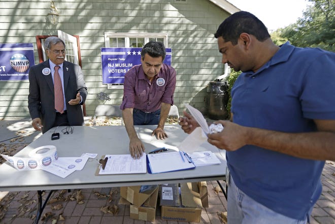 In this Sept. 23, 2016, file photo, Dr. Mohammad Ali Chaudry, left, president of the Islamic Society of Basking Ridge, N.J., and Shawn Butt, center, of Piscataway, N.J., provide voter registration information to Shahul Feroze, right, of South Brunswick, N.J., after a prayer service at the Bernards Township Community Center in Basking Ridge, N.J. The Bernards Township committee voted Tuesday, May 23, 2017, to settle two lawsuits over its denial of a proposed mosque, filed by the U.S. Justice Department and the Islamic Society of Basking Ridge. Some residents say their opposition is because of the selected location, not religious intolerance. THE ASSOCIATED PRESS