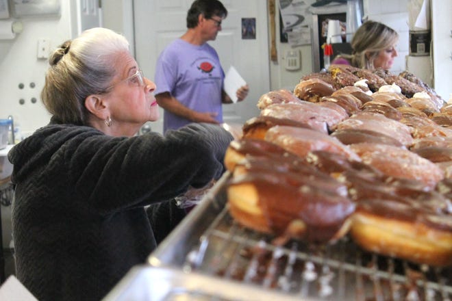 Peggy Pons arranges the freshly made doughnuts in the display case Wednesday morning at Dan-D Donuts & Deli on Harrison Avenue in Panama City. Behind her, son Michael Pons, who has taken over the business, prepares an order. [KATIE LANDECK/THE NEWS HERALD]