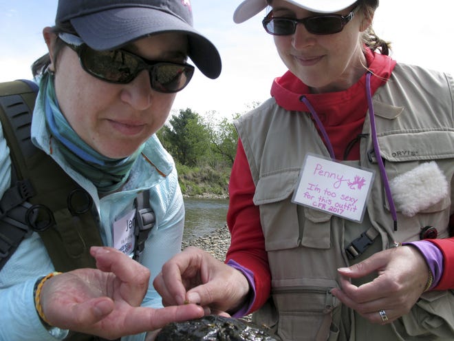 Fly fishers Jen Goodale, left, and Penny Aceto of Fairfax, Vt., show a fly tied to a fishing line in Moscow, Vt. during a fly fishing retreat for breast cancer survivors. The free weekend retreat by Casting for Recovery offers the women counseling, support, medical information, relaxation and fishing. [AP Photo/Lisa Rathke]