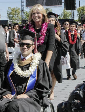 In this May 20 photo, provided by Chapman University, Judy O'Connor pushes her son, MBA graduate Marty O'Connor during commencement at Chapman University in Orange, Calif. Chapman University gave a surprise honorary degree to Judy, after she attended every class and took notes for Marty while he earned a master's degree. [CHAPMAN UNIVERSITY via AP]