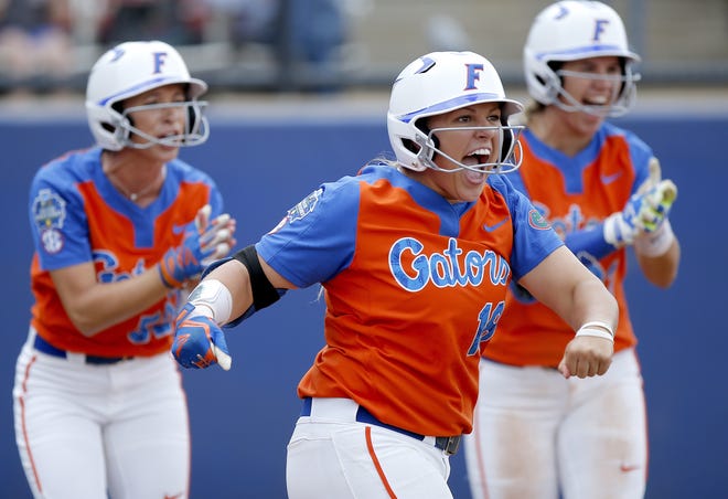 Florida's Amanda Lorenz (18), Justine McLean (52) and Nicole DeWitt (23) celebrate a score in the second inning during the Women's College World Series softball game against Washington in Oklahoma City on Sunday. [Sarah Phipps/The Oklahoman via AP]