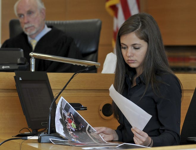 Samantha Boardman, 20, of Norfolk, Mass., a former friend of defendant Michelle Carter looks over photos that were taken at the Homers for Conrad fundraising event that Carter organized several months after Conrad Roy III committed suicide. The trial of Carter proceeds in Taunton District Court in Taunton, Mass., Wednesday, June 7, 2017. She is charged with involuntary manslaughter for encouraging 18-year-old Conrad Roy, III to kill himself in July 2014. [Mark Stockwell/The Sun Chronicle via AP, Pool]