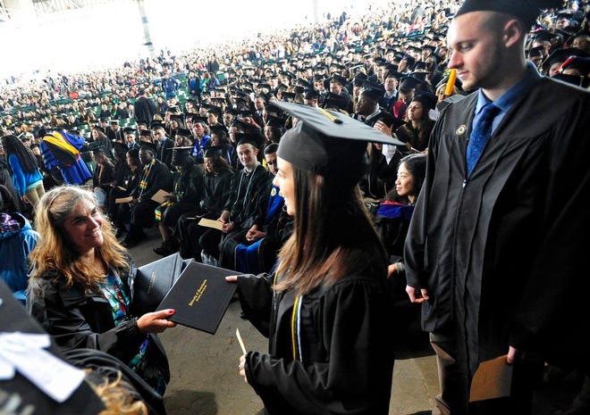 Students are handed their diplomas before walking on stage during graduation at UMass Dartmouth, at the Xfinity Center in Mansfield.