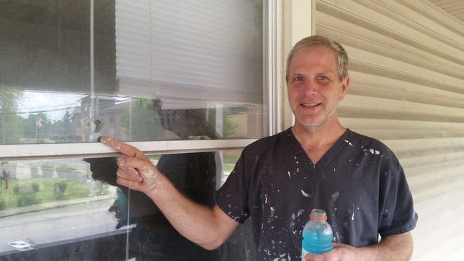 Michael Hoffner points to a bullet hole in the window of a house where he was painting Wednesday at 14th Street NE and Gibbs Avenue. (CantonRep.com / Lori Steineck)