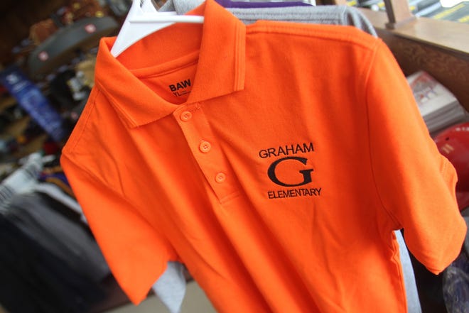 Graham Elementary students have the option of choosing from one of the three polo shirt options from S&M Sports shop on 707 S Lafayette St. Option one is an orange polo with black embroidered Graham logo. [Hannah Dunaway/ The Star]