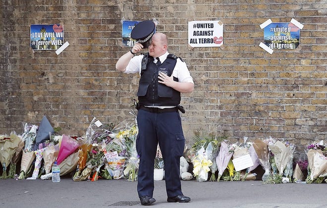A police officer stands near floral tributes in Finsbury Park after an incident where a van struck pedestrians, in London, Monday. British authorities and Islamic leaders moved swiftly to ease concerns in the Muslim community after a man plowed his vehicle into a crowd of worshippers outside a north London mosque early Monday, injuring at least nine people. [FRANK AUGSTEIN/ASSOCIATED PRESS]