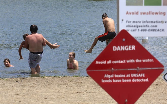 Swimmers take to the water Monday despite a sign posting the danger of contact with the water at Crystal Beach at Buckeye Lake. High levels of toxic algae were recorded in the water off of two beaches there. [Eric Albrecht/Dispatch]