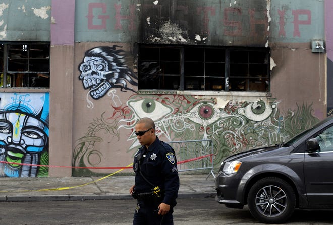 File - In this Dec. 9, 2016 file photo, an Oakland police officer guards the area in front of the art collective warehouse known as the Ghost Ship in the aftermath of a fire in Oakland, Calif. More than six months after the Dec. 2 blaze at the warehouse that authorities said was illegally converted into living quarters, the Oakland Fire Department has released a 50-page report filled with harrowing details of death and panic as the flames and deadly smoke spread. The report contains many previously unknown details about the nation's deadliest structure fire in more than 14 years and says investigators could not determine the cause of the blaze due to extensive fire damage.(AP Photo/Ben Margot)