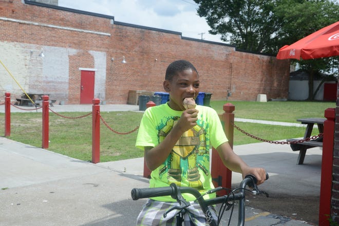 Lavonta Carter,12, cools off with an ice cream cone Monday as he rides his bicycle along North Street. Temperatures in the high 90's heated up Kinston and Lenoir County. [Janet S. Carter / The Free Press]