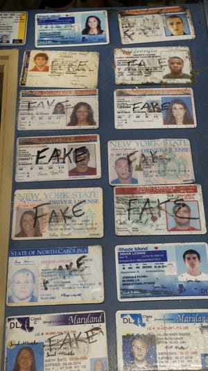 Confiscated fake IDs decorate the checkout counter of Bridge Liquors in Newport. The store has posted on its webpage about its efforts to catch the high number of underage drinkers who try to fake their way to a six pack. [The Providence Journal / Kris Craig]