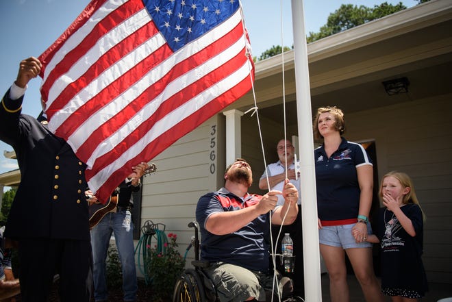 Veteran and double amputee Eric Myers raises the American flag in front of his new smart home on Thursday in Linden. Myers' family was given the home by the Stephen Siller Tunnel to Towers Foundation, an organization that is named after a firefighter who was killed on 9/11. [Andrew Craft/The Fayetteville Observer]