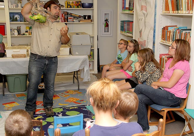 Brendan Finerty, owner of Wild World Zoo, in Jackson, shows a group of children how a Double Yellow-Headed Amazon Parrot can hang upside down to get its food. The presentation was part of the Jonesville District Library's summer reading program. [ANDY BARRAND PHOTO]