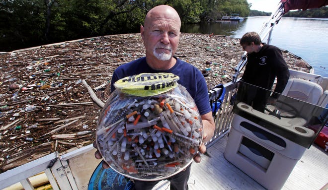 n this Wednesday June 7, 2017 photo, activist Rocky Morrison, of the "Clean River Project", holds up a fish bowl filled with hypodermic needles, that were recovered during 2016, on the Merrimack River next to their facility in Methuen, Mass.