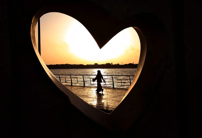 In this May 11, 2014, file photo, a Saudi woman seen through a heart-shaped statue walks along an inlet of the Red Sea in Jiddah, Saudi Arabia. A young Saudi woman has sparked a sensation online by posting a video of herself in a miniskirt and crop top walking around in public, with some Saudis calling for her arrest and others rushing to her defense. The video, first shared on Snapchat, shows her walking around an empty historic fort in Ushaiager, a village north of the capital, Riyadh, in the desert region of Najd, where many of Saudi Arabia's most conservative tribes and families are from.