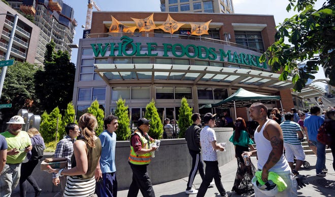 In this Tuesday, July 11, 2017, photo, pedestrians walk past a Whole Foods Market, just down the street from the headquarters of Amazon, in Seattle. Amazon, already a powerhouse in books, shoes, streaming video, electronics and just about everything else, will bind its customers even more closely once it completes its $13.7 billion bid for the organic grocer Whole Foods. Although antitrust lawyers believe the deal will get approved, many customers and experts alike worry about two big companies combining into a bigger one. (AP Photo/Elaine Thompson)