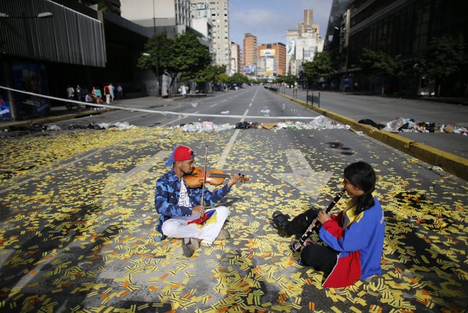 Musicians play their instruments as they sit in the middle of a road littered with metro tickets at a roadblock set up by anti-government protesters in Caracas, Venezuela, Thursday, July 20, 2017. Venezuelan President Nicolas Maduro and his opponents face a crucial showdown Thursday as the country's opposition calls a 24-hour national strike. The country's largest business group, Fedecamaras, has cautiously avoided full endorsement of the strike, but its members have told employees that they won't be punished for coming to work. (AP Photo/Ariana Cubillos)