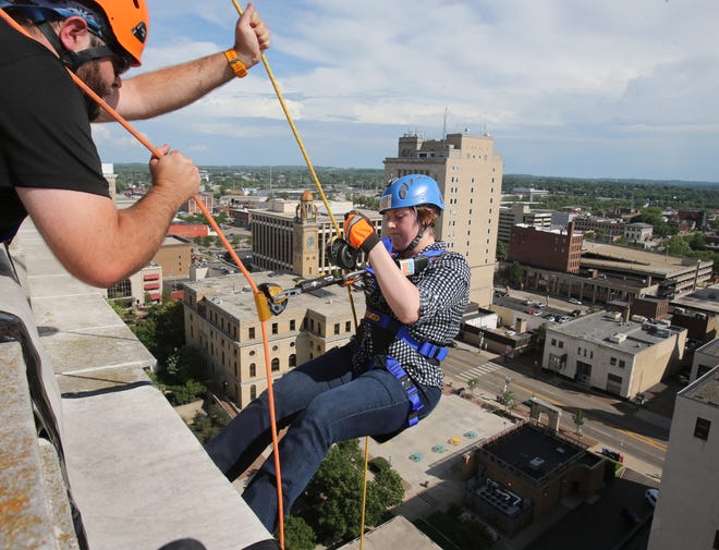 Kelly Byer, a reporter with The Canton Repository, is assisted by Kevin Kissell as she begins to rappel down the side of the Onesto Lofts in Canton. (CantonRep.com / Scott Heckel)