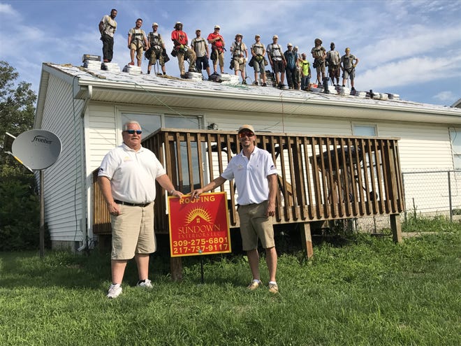 Ed Lenhardt, left and Zack Vest owners of Sundown Exteriors stand on the ground as their crew is seen atop Don Hatfield’s roof in Lincoln. [Photo by Jean Ann Miller/The Courier]