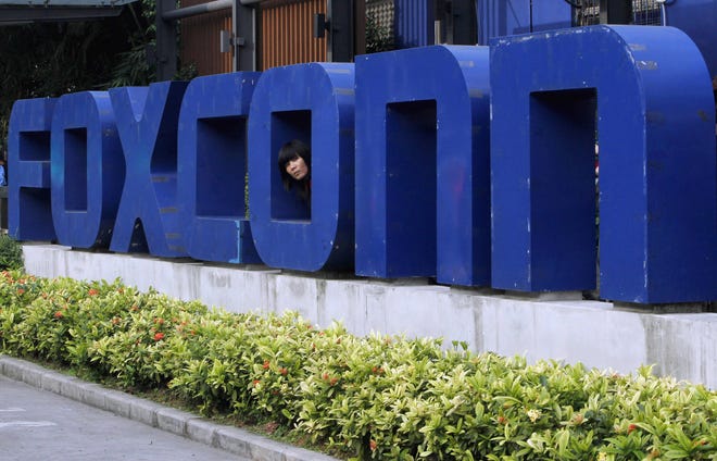 In this May 27, 2010 file photo, a worker looks out through the logo at the entrance of the Foxconn complex in the southern Chinese city of Shenzhen. Conservationists are lining up to oppose Republican plans to eliminate key environmental regulations as part of an incentive package to lure a $10 billion Foxconn electronics plant to southeastern Wisconsin. Gov. Scott Walker’s incentives bill would exempt the company from environmental impact statements and state permits for filling wetlands and building on lake beds. (AP Photo/Kin Cheung, File)