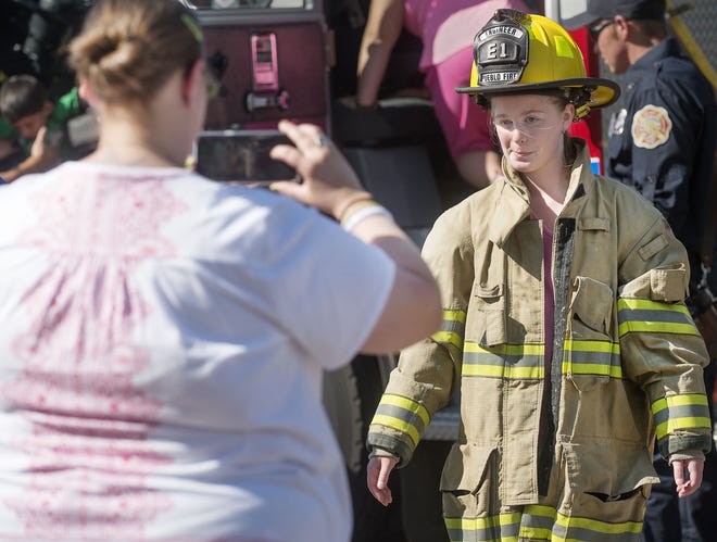 CHIEFTAIN PHOTOS/BRYAN KELSEN KyAn Duewiger, 11, gets her photo taken by her mother Brandy Duewiger as she tries on a bunker coat and fire helmet at the Neighborhood Safety Night at the Historic Arkansas Riverwalk of Pueblo Tuesday.