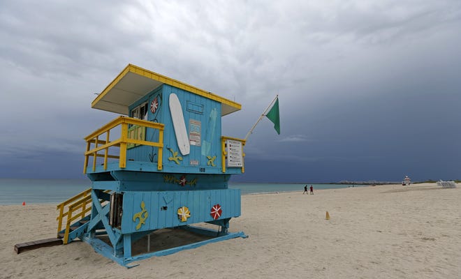 In this Friday, July 28, 2017, photo, two young men walk along the beach covered by rain clouds in the South Beach area of Miami Beach. Tropical Storm Emily began trekking east across the Florida peninsula on Monday, scattering drenching rains amid expectations it would begin weakening in the coming hours on its approach to the Atlantic coast. (AP Photo/Alan Diaz)