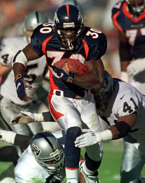 Denver Broncos running back Terrell Davis breaks through Oakland Raiders tacklers Terry Wooden, bottom, and Louis Riddick (41) for first down yardage during first quarter action at Mile High Stadium in Denver on Sunday, Nov. 22, 1998. (AP Photo/David Zalubowski)