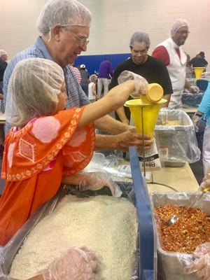 Lillian Robinson, 9, pours a scoop of rice into a funnel while another person holds a bag for the ingredients for a package meal for Rise Against Hunger on Sunday, Aug. 6, 2017, at Holy Trinity Lutheran Church in Gastonia. [Alyssa Pressler/The Gaston Gazette]
