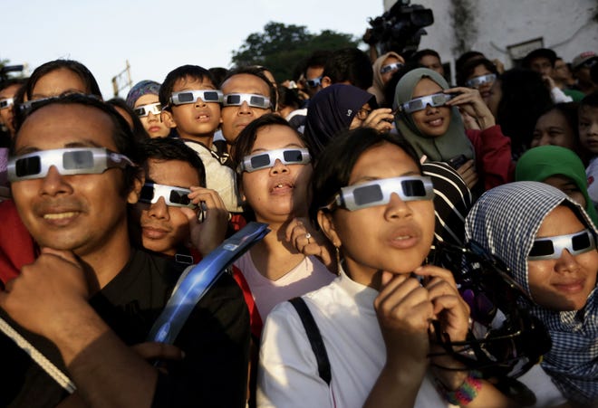 In this 2016 file photo, people wearing protective glasses look up at the sun to watch a solar eclipse in Jakarta, Indonesia. Doctors say not to look at the sun without eclipse glasses or other certified filters except during the two minutes or so when the moon completely blots out the sun, called totality. That's the only time it's safe to view the eclipse without protection. When totality is ending, then it's time to put them back on. [Dita Alangkara, Associated Press]