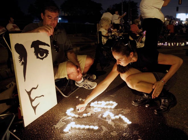 FILE- This Aug. 15, 2010 file photo shows Melanie Curry as she lights candles at an Elvis Presley display she made with Judd Cannon, left, on Elvis Presley Boulevard in front of Graceland, Presley’s Memphis, Tenn. home. Friends and fans of late singer and actor Elvis Presley are descending on Memphis, Tennessee, for Elvis Week, the annual celebration of his life and career. It coincides with the 40th anniversary of the passing of Presley, who died on Aug. 16, 1977. (AP Photo/Mark Humphrey, File)