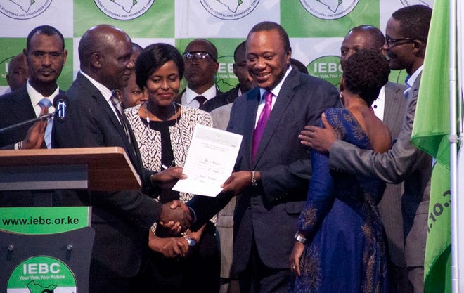 The Chairman of the Independence Electoral and Boundaries Commission, Wafula Chebukati , left, hands over the certificate to Uhuru Kenyatta, centre right, after announcing him the winner in the presidentail race at the Centre in Bomas, Nairobi, Kenya, on Friday. The commission said Kenyatta won Tuesday's election with 54 percent of the vote. It called the vote "credible, fair and peaceful."