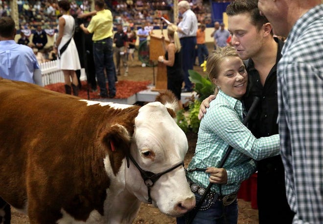 Land of Lincoln Grand Champion Steer winner Taylor Donelson of Clinton gets a hug from American Idol winner Scotty McCreery after McCreery egged on Gov. Bruce Rauner, far right, who placed the top bid of $61,000 for the steer during the Governor's Sale of Champions auction at the Illinois State Fair on Tuesday, Aug. 18, 2015. David Spencer/The State Journal-Register