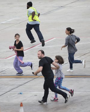 In this Jan. 6, 2017 file photo, people run on the tarmac after a gunman opened fire in the baggage claim area at Fort Lauderdale-Hollywood International Airport, in Fort Lauderdale. A report released Tuesday, Aug. 15 says that law enforcement command and communication systems broke down following last January's deadly shooting at the Florida airport, leading to confusion and eventually panic as a false report of a second gunman spread among officers, passengers and employees. (AP Photo/Wilfredo Lee, File)