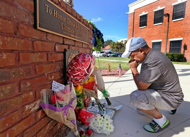 After placing flowers at a makeshift memorial, Miguel Velez say's a prayer for the officer that was killed on Saturday in Kissimmee, Fla. The Kissimmee Police Department says Sgt. Sam Howard died Saturday from his injuries. His colleague, Officer Matthew Baxter, died Friday night after the attack in a neighborhood of Kissimmee, located south of the theme park hub of Orlando.