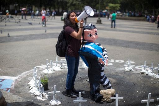 Activist Andrea Ixchiu holds an effigy of Guatemala's President Jimmy Morales and shouts slogans in support of Ivan Velasquez, chief of a U.N. anti-corruption commission, in the middle of an altar honoring dozens of girls who died in a fire at a children's home this year, in the Central Plaza of Guatemala City, Monday, Aug. 28, 2017. Morales ordered Velasquez to leave the country after he and Guatemala's attorney general called for the removal of the president's immunity from prosecution, so they can pursue an investigation into alleged campaign finance violations. (AP Photo/Luis Soto)