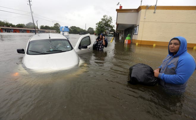 Conception Casa, center, and his friend Jose Martinez, right, check on Rhonda Worthington after her car become stuck in rising floodwaters from Tropical Storm Harvey in Houston, Texas, Monday, Aug. 28, 2017. The two men were evacuating their home that had become flooded when they encountered Worthington's car floating off the road. (AP Photo/LM Otero)