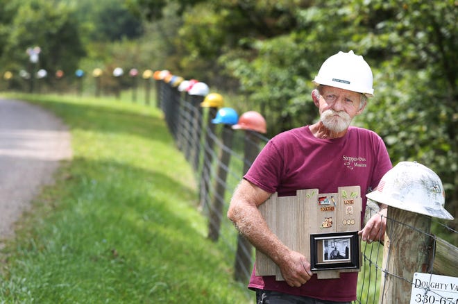 TIMES-REPORTER PAT BURK

Rusty Walters, wearing his father Clyde Walters' hard hat and holding a plaque with his photo, stands next to his hard hat on the Hard Hat Memorial Fence he created at his home near Midvale.