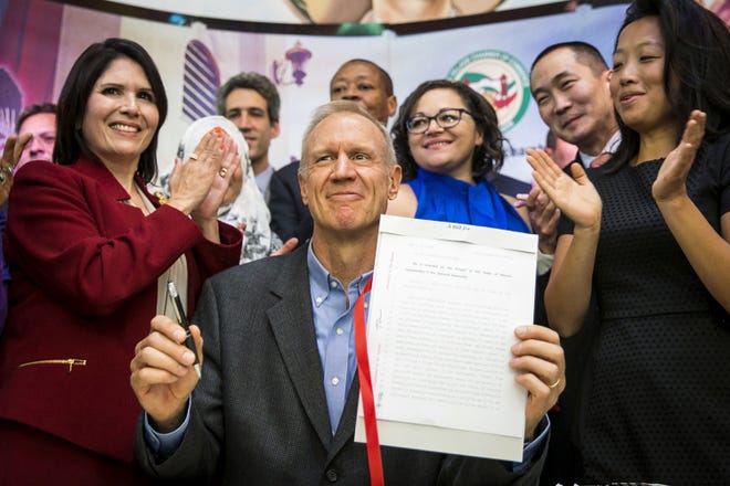 Illinois Gov. Bruce Rauner smiles while surrounded by law enforcement officials and immigrant rights activists in Chicago's Pilsen neighborhood Monday, Aug. 28, 2017, after signing legislation that will limit how local and state police can cooperate with federal immigration authorities. The narrow measure prohibits police from searching, arresting or detaining someone solely because of immigration status, or because of so-called federal immigration detainers. (Ashlee Rezin/Chicago Sun-Times via AP)