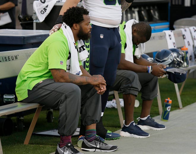 FILE - This Thursday, Aug. 31, 2017 file photo Seattle Seahawks defensive end Michael Bennett, left, sits during the playing of the national anthem next to Justin Britt, center, and another teammate before an NFL preseason football game between the Raiders and the Seattle Seahawks in Oakland, Calif. Bennett is accusing Las Vegas police of racially motivated excessive force when he says he was detained at gunpoint on Aug. 27, 2017, handcuffed and later released without charges following a report that gunshots were heard at a casino hotel. (AP Photo/Eric Risberg,File)
