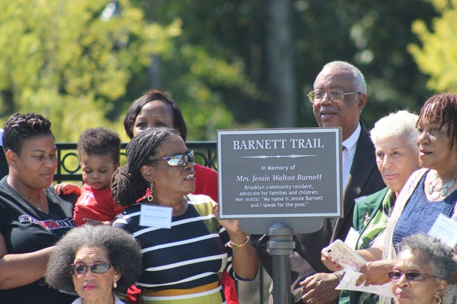 Barbara Barnett, center, is the daughter of the late Jessie Walton Barnett for whom Barnett Trail in Columbia Brookside was named. Above, Barnett admires a replica of the plaque that sits at either end of Barnett Trail dedicating the stretch of road to the Athens community leader. (Photo by Red Denty / Staff)