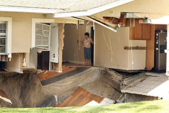 Ellen Miller carefully surveys the damage as her home at 222 West Kelly Park Road in Apopka, Fla., that is being swallowed by a sinkhole on Tuesday, Sept. 19. Orange County Fire Rescue spokeswoman Kat Kennedy says crews responded Tuesday morning, shortly after the Apopka house began sinking. She says the sinkhole measured about 20 feet across and 15 feet deep. No injuries were reported to the home's residents. Kennedy says they're staying with relatives. [STEPHEN M. DOWELL / ORLANDO SENTINEL ]