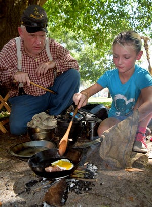 Charlie Harvell of Rocky Mount, a member of the 13th Virginia, shows homeschooler Shyann Faucette of New Bern how to cook over an outdoor fire during Civil War Weekend at New Bern Academy. [CHARLIE HALL / SUN JOURNAL]