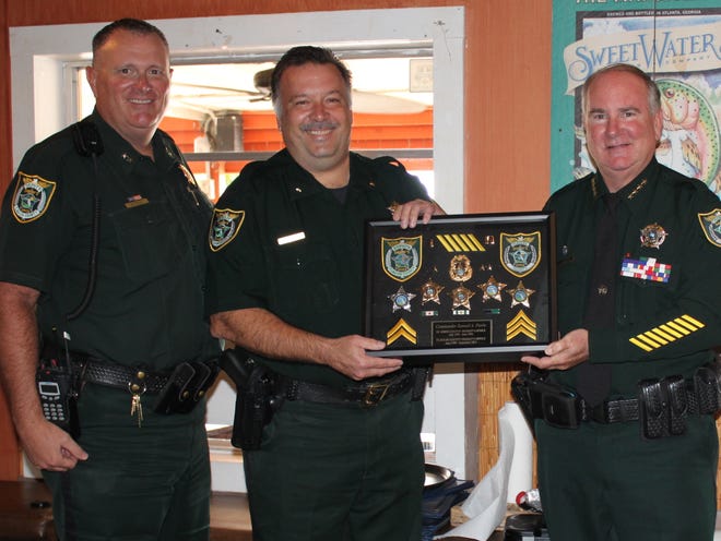 Retiring after 21 years, Flagler County Sheriff's Office Commander Sam Ferris, center, accepts a shadow box displaying his various badges earned over the years from Sheriff Rick Staly while Chief Steve Cole, left, stand by during a luncheon Tuesday in Ferris's honor. [Photo provided/FCSO]