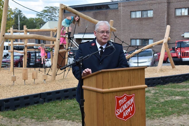 Maj. Brian Gilliam speaks at the playground dedication ceremony Tuesday at the Salvation Army as children enjoy the new play area in the background. [REBECCA WALTER/TIMES-NEWS]