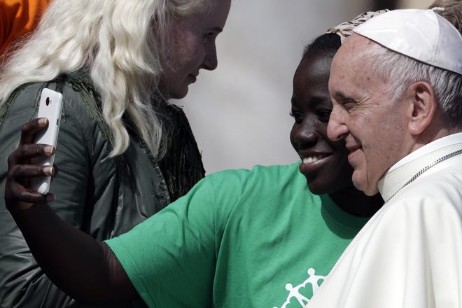 Pope Francis takes a selfie with a migrant during his weekly general audience, at the Vatican Wednesday. The pope has launched a two-year activism and awareness-raising campaign about the plight of migrants to counteract mounting anti-immigrant sentiment in the U.S., Europe and beyond. [ANDREW MEDICHINI/AP PHOTO]