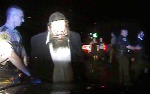 In this Aug. 8, 2017, still frame from dashboard camera video released by the Vermont State Police, Trooper Justin Thompson, left, detains driver Rabbi Berl Fink, while a second officer, right, detains passenger Rabbi Eli Fink, both of of Brooklyn, N.Y., during a traffic stop in Thetford, Vt. An internal investigation of the nighttime traffic stop of the rabbi, who was ordered at gunpoint to the ground and his family handcuffed after he failed to stop, has cleared the trooper of wrongdoing. State police officials said Friday, Sept. 29, 2017, that Thompson clocked the vehicle at 83 miles per hour on Interstate 91, and he tried to stop the vehicle with lights and siren but it failed to stop for 4.5 miles. (Vermont State Police via AP)