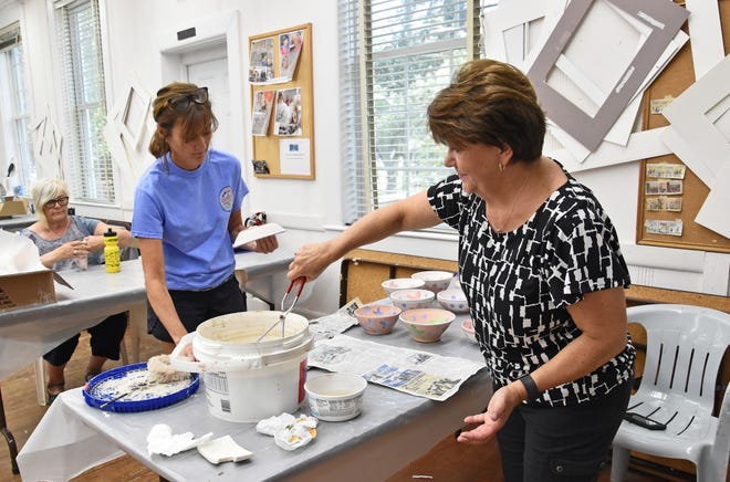 Mary Beth Johnson (right), event chair of the Empty Bowls fundraiser in Southport, dips a painted bowl into a clear glaze, while committee member Kathy Scheetz gets the next bowl ready to be dipped. [CAROLYN BOWERS/FOR THE STARNEWS]