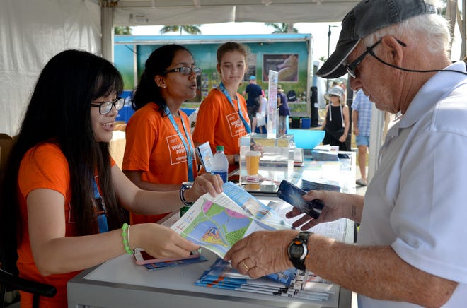 Volunteers, from left, Mai Tran of Tampa, Sri Meghana Kopparthi of Jacksonville and Ansley Gibson, also of Jacksonville, help out at the infomation booth as Gid Pool of North Port picks up a fan guilde on Friday during the 2017 World Rowing Championships at Nathan Benderson Park in Sarasota. [HERALD-TRIBUNE STAFF PHOTO / MIKE LANG]
