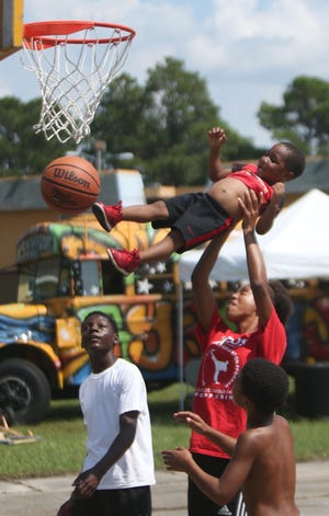 Journey Venible, 16, lifts a little boy to help him try to reach the hoop at Macedonia Garden Apartments on Saturday. Several community groups hosted a three-on-three basketball tournament and gathering at the complex to promote healthy activites for the youth. [PATTI BLAKE/THE NEWS HERALD]