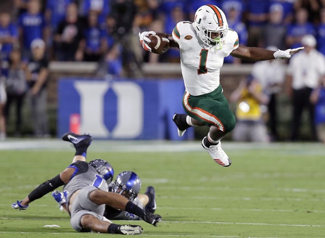 Miami's Mark Walton, right, jumps over Duke's Ben Humphreys and Bryon Fields Jr. during the first half of a game on Sept. 29 in Durham, N.C. [AP Photo / Gerry Broome]